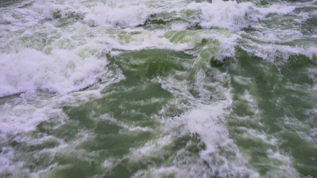 A Close-up View of Turbulent River Rapids with White Foam and Greenish Water. High quality 4k footageA dynamic close-up shot captures the powerful motion of churning river water filled with white foam