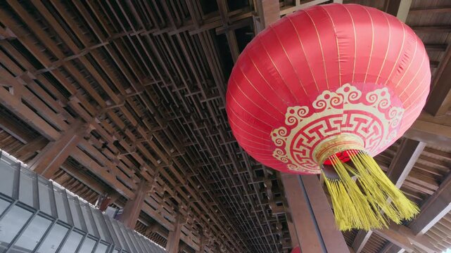 A large red Chinese lantern hangs beneath an intricate wooden ceiling in a traditional temple interior, highlighting cultural architecture, festive decoration and ornamental craftsmanship in warm