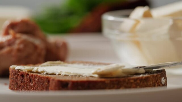 Young woman spreading nut butter on rye black bread toast in kitchen, closeup