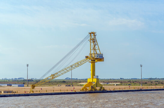 Large yellow harbor portal crane standing at an industrial port terminal against a clear blue sky, designed for heavy cargo handling and maritime logistics operations