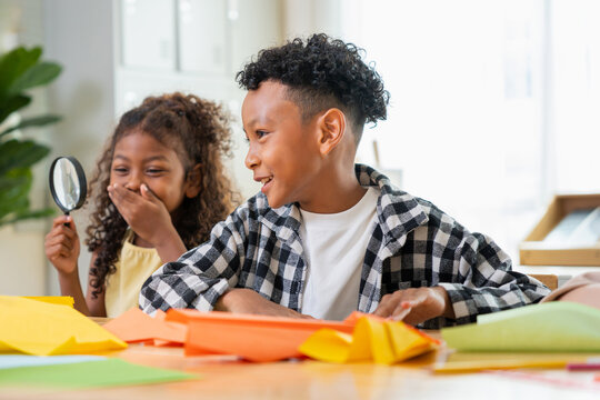 Happy multiethnic school children playing with magnifying glass and paper craft in classroom, cheerful kids having fun in modern classroom with school supplies and magnifying glass