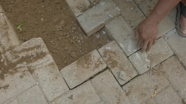 Hands installing interlocking paving blocks in a puzzle-like pattern after dismantling the previous surface, showing construction work, pavement repair, landscaping, and outdoor renovation.