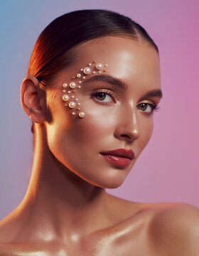 Beautiful young woman wearing elegant pearl facial makeup and glowing skin against vibrant colored background