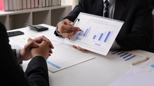 Professional colleagues discussing business strategy and analyzing financial data with charts and graphs during a corporate meeting in the office.
