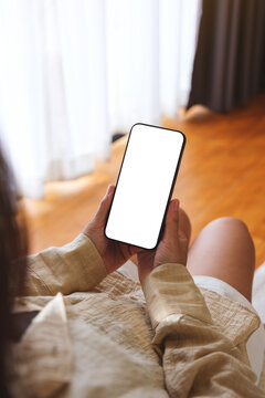 Vertical mockup image of a woman holding and using mobile phone with blank desktop white screen at home