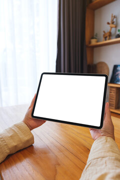 Vertical mockup image of a woman holding tablet with blank desktop white screen at home