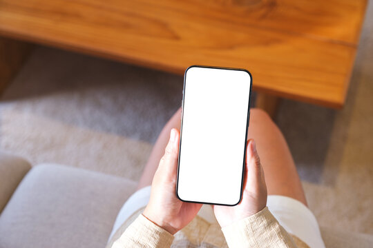 Top view mockup image of a woman holding and using mobile phone with blank desktop white screen at home