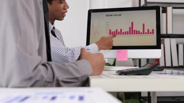Financial advisors discussing book value chart on computer screen.