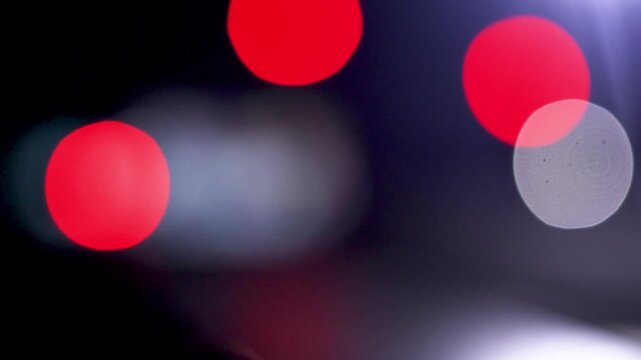 Abstract static shot of out of focus large vibrant red bokeh orbs against dark background.