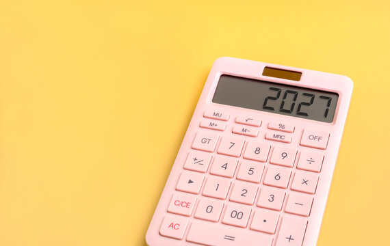 Pink calculator displaying 2027 on bright yellow background with copy space. Annual financial planning, budgeting, expense management, savings goals and personal or business finance preparation.