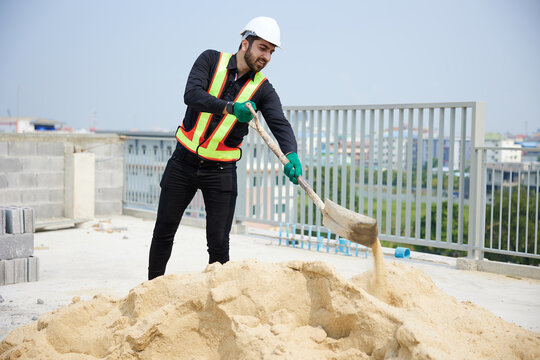 Construction worker is shoveling sand on a sunny day. He is in the process of building something new.