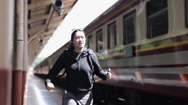 Asian woman running late for her train. Panicked Asian woman with a backpack running along a train platform. Young female tourist rushing to catch her departing train.
