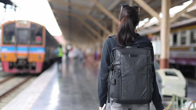 Woman with backpack and luggage walking on a train station platform.