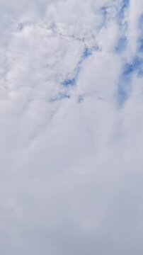 Vertical timelapse of clouds drifting across a bright cloudy sky with subtle patches of blue, creating a peaceful atmospheric nature background.