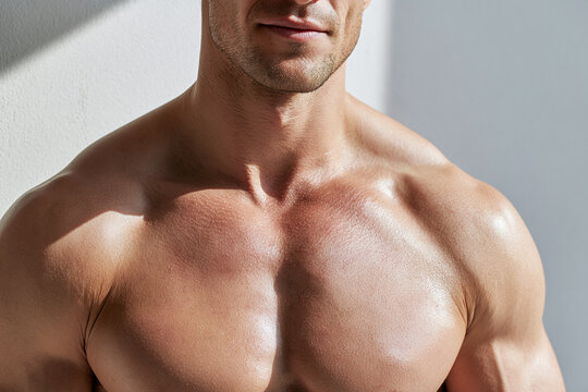 Athletic male torso leaning against wall with sunlight highlighting muscular chest and shoulder, warm skin tone and subtle shadow creating confident, focused mood