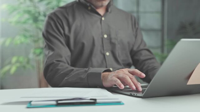 Focused employee conducts business research typing keyboard keys as corporate business analysis guides online research beside paperwork.