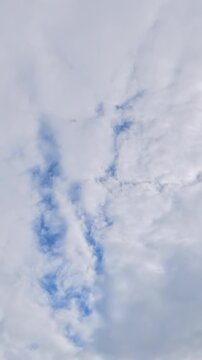 Vertical timelapse of soft clouds drifting across a bright cloudy sky with subtle blue patches, creating a peaceful atmospheric nature background.