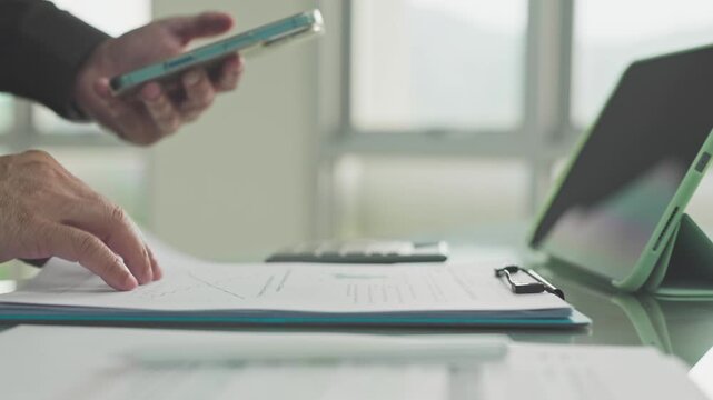 Executive conducts financial analysis across reports, ensuring careful analysis during paperwork audit procedures beside digital tablet devices.