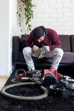 Repairman inspecting broken vacuum cleaner part while sitting on couch at home