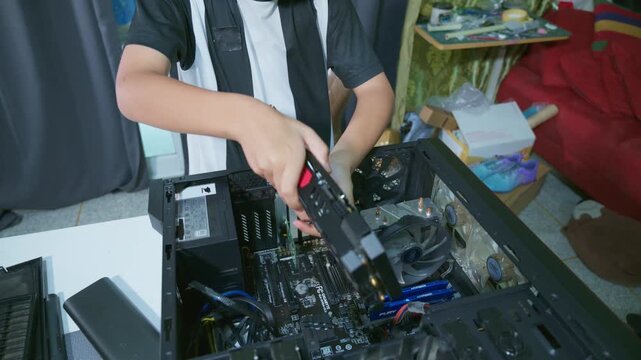 Young boy concentrating while repairing and assembling hardware inside an open desktop computer case at home, learning technology and problem solving skills
