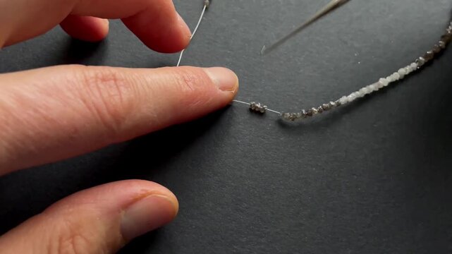 Hands carefully threading small beads onto a string for jewelry making