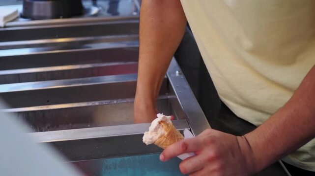 Street vendor hands scooping fresh ice cream into a waffle cone