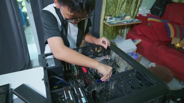 Young boy concentrating while repairing and assembling hardware inside an open desktop computer case at home, learning technology and problem solving skills