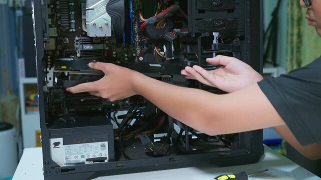 Young boy concentrating while repairing and assembling hardware inside an open desktop computer case at home, learning technology and problem solving skills