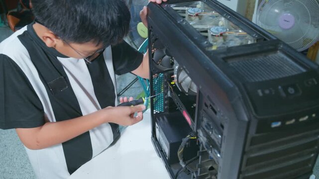 Young boy concentrating while repairing and assembling hardware inside an open desktop computer case at home, learning technology and problem solving skills