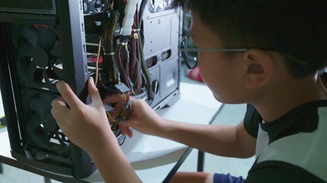 Young boy concentrating while repairing and assembling hardware inside an open desktop computer case at home, learning technology and problem solving skills