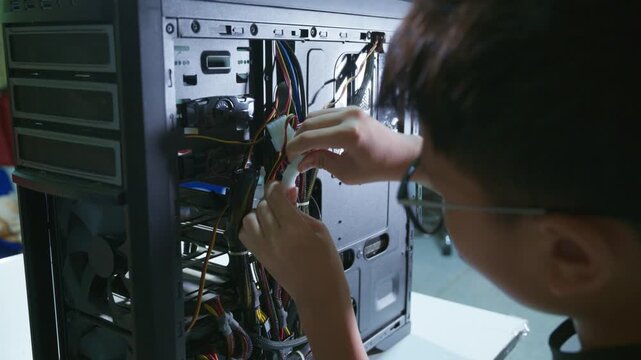 Young boy concentrating while repairing and assembling hardware inside an open desktop computer case at home, learning technology and problem solving skills