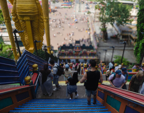 Tourists Walking Up and Down Colorful Steps at Batu Caves Temple Complex in Malaysia with Large Golden Statue