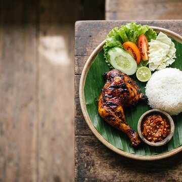 Traditional Indonesian grilled chicken served with steamed rice and fresh vegetables on a banana leaf.
