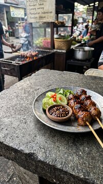 Traditional Indonesian chicken satay skewers served on a plate with fresh cucumber slices and spicy soy sauce.