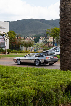 Silver DMC DeLorean sports car rear three-quarter view on road near scenic mountain background