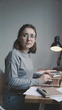Vertical 4K video female developer in glasses thinks then has sudden insight turns back to laptop and types very fast, concept of idea problem solving and coding breakthrough