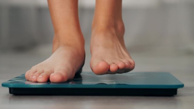 Close-up of woman stepping barefoot onto a digital bathroom scale to check body weight, illustrating weight loss progress, dieting and weight management at home.