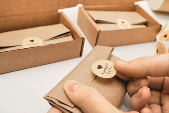 Close-up of hands sticking thank you sticker to craft paper package for shipping