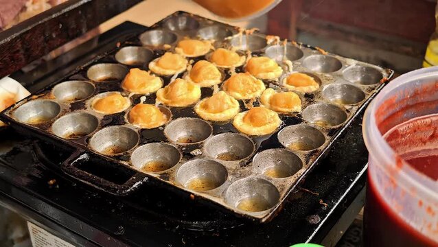 Street vendor cooking fried egg tapioca balls cilor in a special round hole frying pan with bamboo skewers at local market. 4K