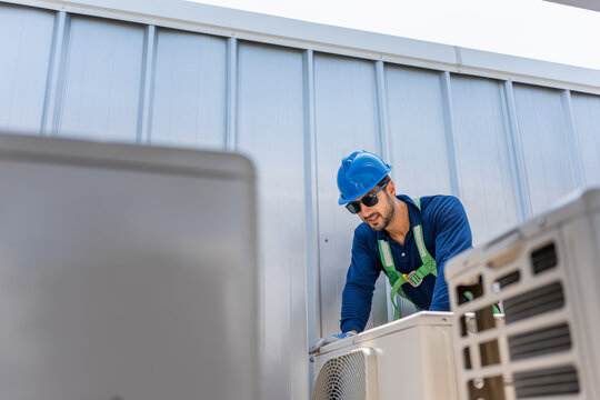 Engineer man performing quality check on industrial air conditioning unit on rooftop exterior, Professional HVAC technician checking air conditioning condenser unit on rooftop during maintenance