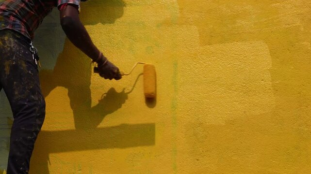 Person painting an outdoor wall with yellow paint