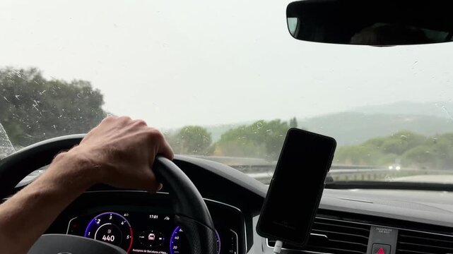 Driver hand on steering wheel driving on rainy highway with windshield wipers