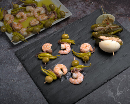 Assortment of traditional Spanish tapas skewers featuring pickles, boiled egg, tuna, olives, anchovies, and prawns served on rectangular plates