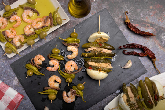 Assortment of traditional Spanish tapas skewers featuring pickles, boiled egg, tuna, olives, anchovies, and prawns served on rectangular plates