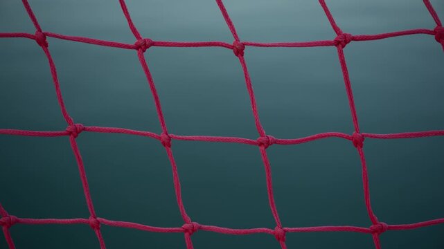 Close-up of a red water polo goal net showing knot details against a deep blue water background. 4K.