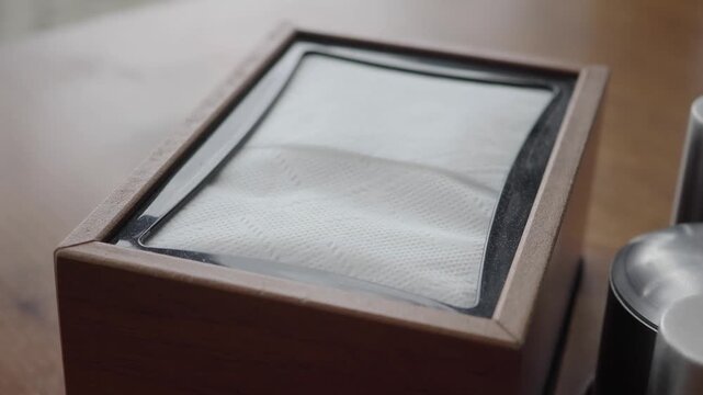 Tissue box on wooden table with silverware and napkin holder