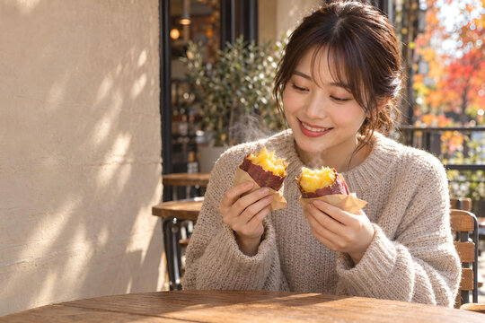 焼き芋の湯気と甘い香りに笑顔がこぼれる日本人女性、秋のカフェテラスで楽しむ旬のおやつと広告用余白-生成