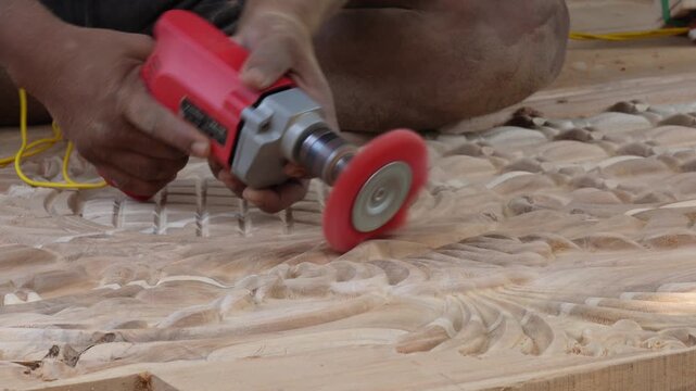 Worker smoothing carved wood with an electric rotary abrasive brush