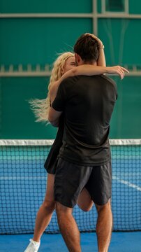 A couple embracing joyfully on a blue indoor tennis court after a match in athletic sportswear
