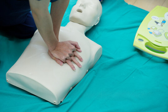 Healthcare trainees practicing chest compressions and airway management with AED pads applied to a patient simulator. 